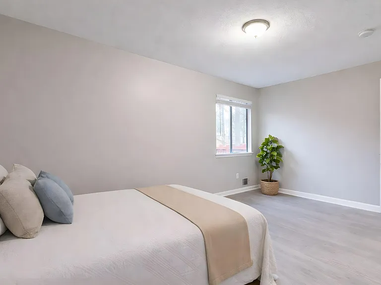 Spacious bedroom with neutral finishes, wide-plank flooring, and a large window for natural light and fresh air.