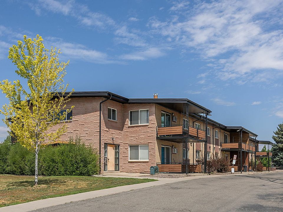 Charming apartment building with eye-catching brick facade, surrounded by lush greenery and a clear blue sky, offering modern living in a serene neighborhood.