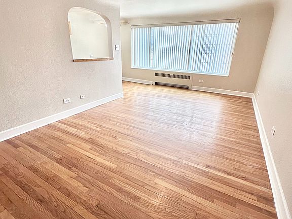 Bright living room with warm hardwood floors and large window for natural light, creating an inviting and spacious atmosphere.