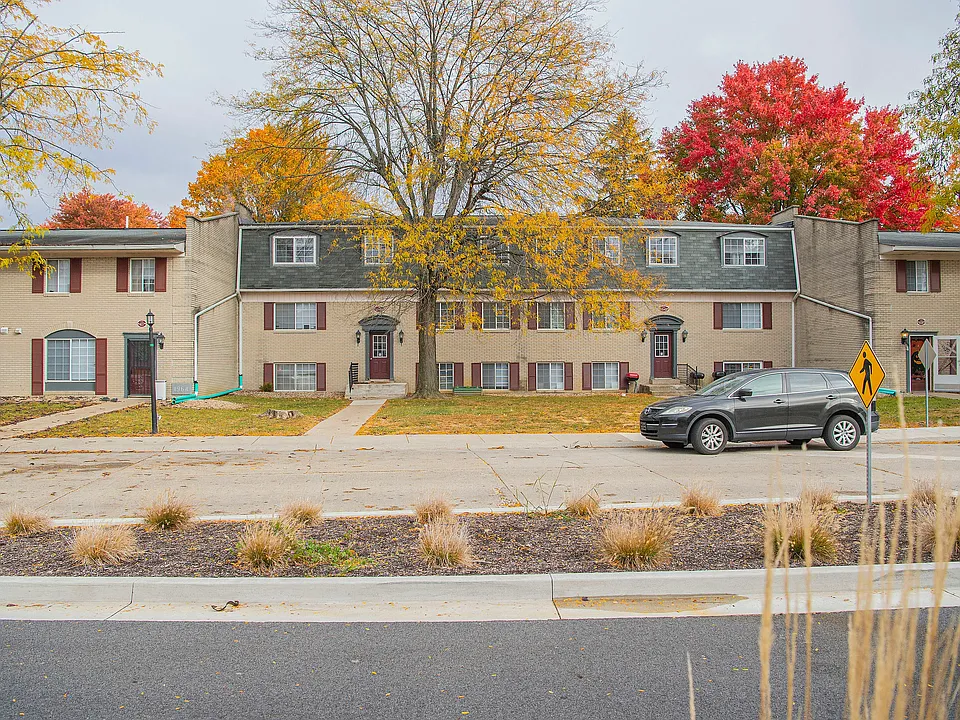 Elegant apartment building surrounded by vibrant autumn trees, featuring charming brickwork and inviting entrances, perfect for comfortable suburban living.
