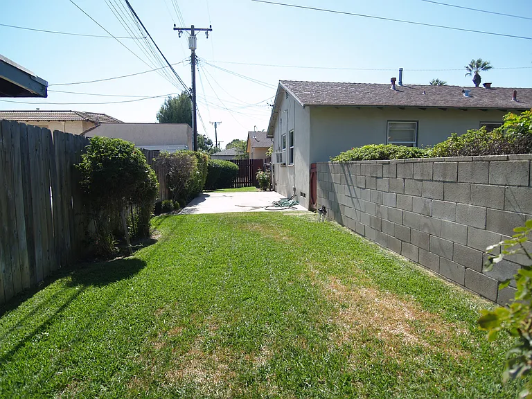 Separate fenced in yard with auto sprinklers and cement slab.