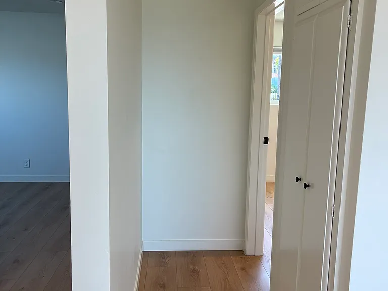 View from living room down hallway to smaller bedroom. Note coat closet and cupboards in hallway.
