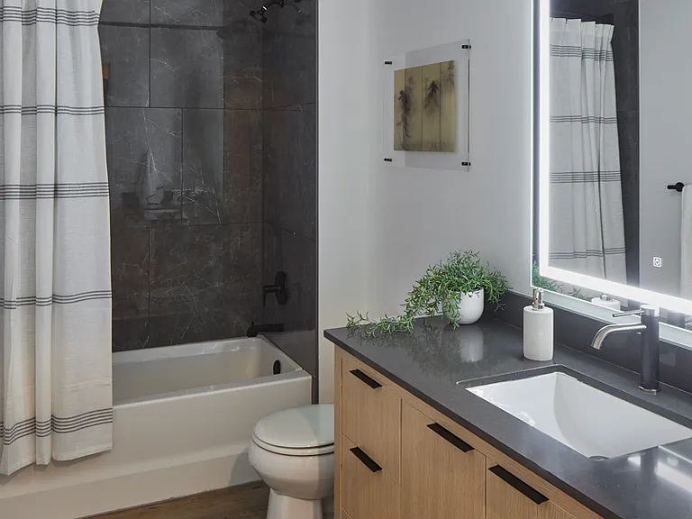 Apartment bathroom with wood-style flooring and LED vanity mirror.
