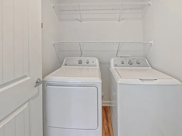 Modern laundry room featuring sleek white washer and dryer with overhead shelving for storage.