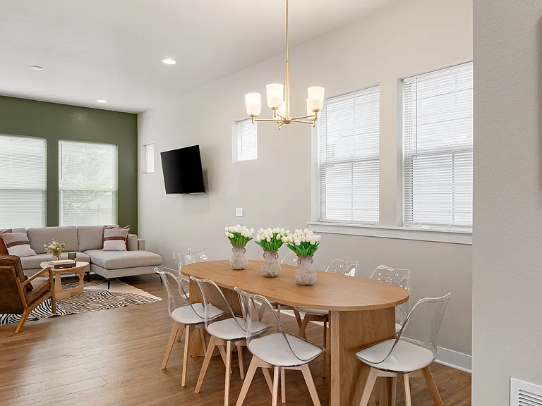 Relax in a cozy living area with a comfortable sectional sofa and stylish armchair. The dining space features a wooden table with clear chairs, perfect for meals or gatherings, all illuminated by natural light from large windows.