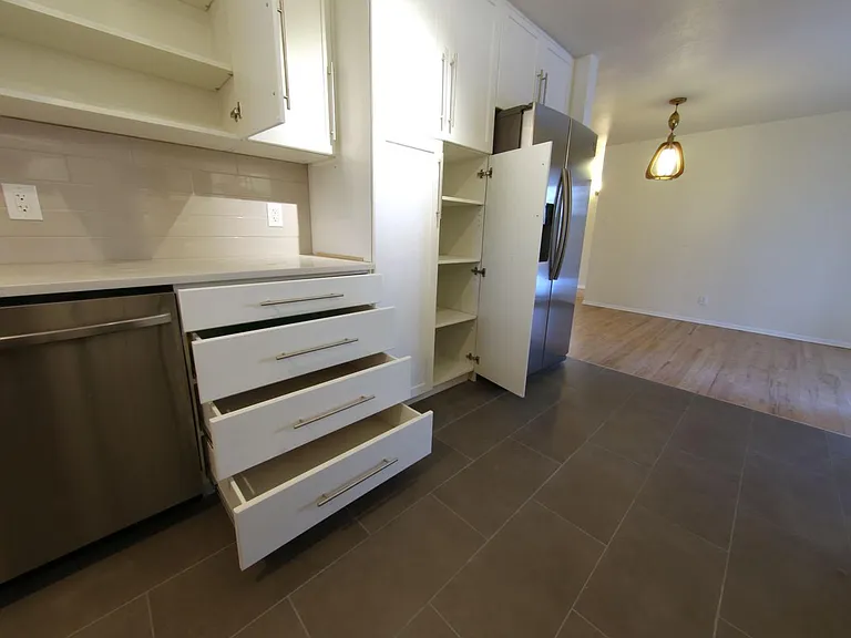 Pantry open next to fridge, with shelves and cabinets extended. Ample storage in this highly-functional kitchen.