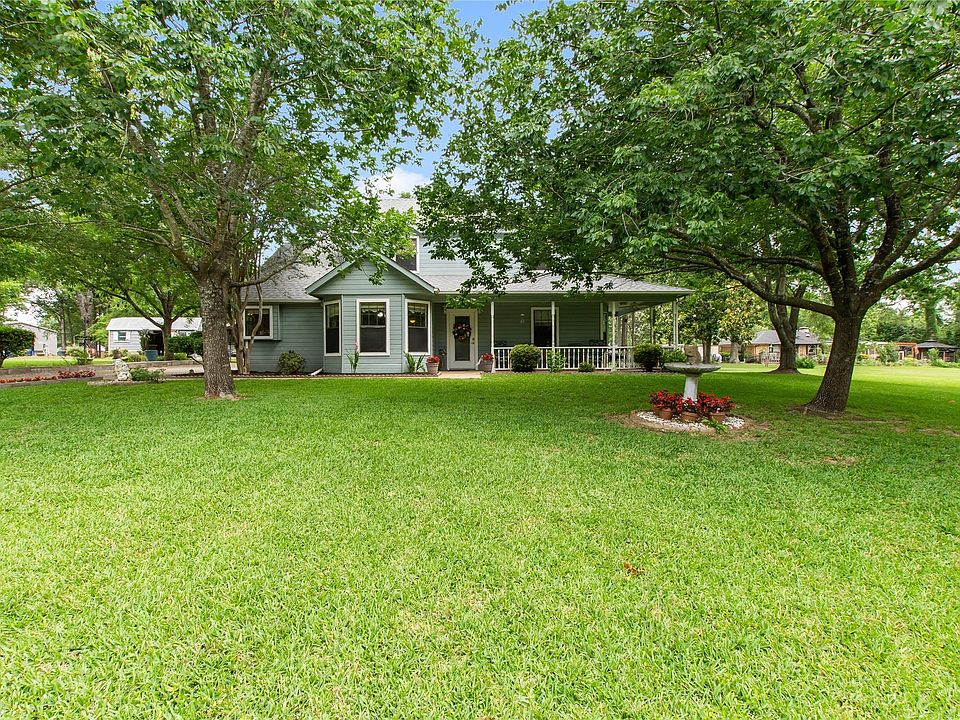 Charming country-style home nestled beneath mature shade trees with a welcoming wraparound porch and beautifully maintained lawn offering exceptional curb appeal.