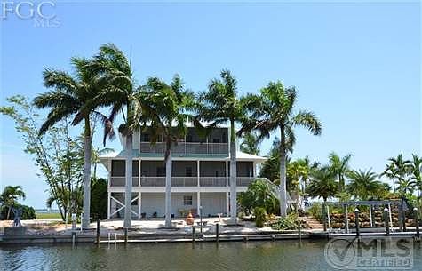 The rear view of home with mature Royal Palm trees, 2 screened decks, dock along seawall and boat lift with wrap around dock.