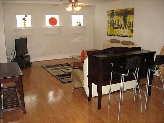 A view of the living area, which has wood flooring and a ceiling fan, along with 3 niche windows tha