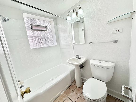 Bright and modern bathroom with a clean white aesthetic, featuring a sleek bathtub, pedestal sink, and elegant lighting.