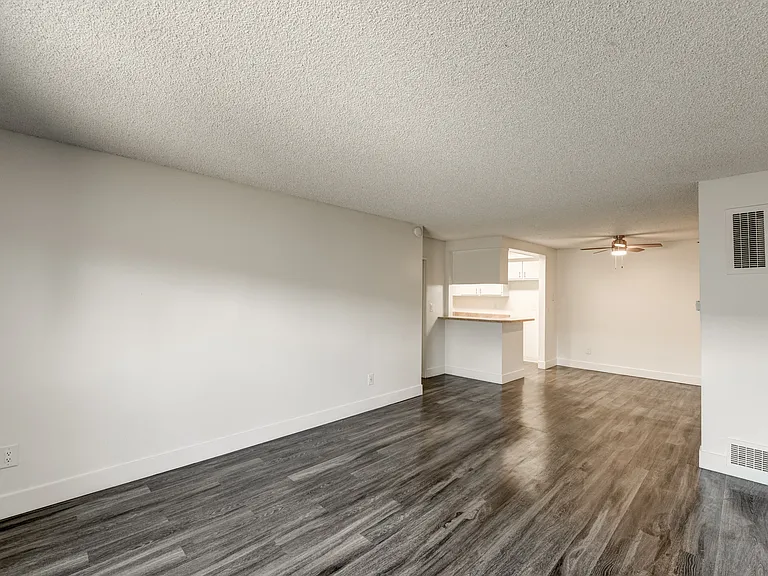 an empty living room and kitchen with wood flooring and a ceiling fan