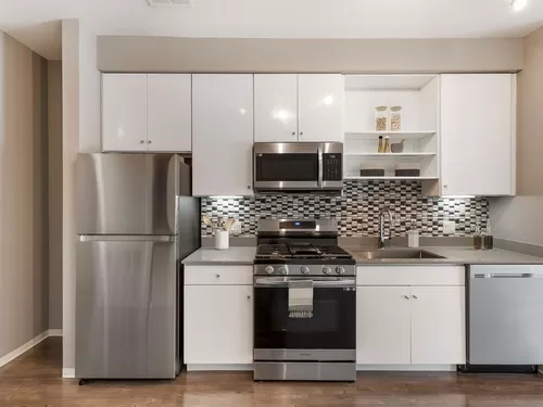Renovated Package I kitchen with stainless steel appliances, dark quartz countertops, white cabinetry, tile backsplash, and hard surface flooring - AVA Somerville