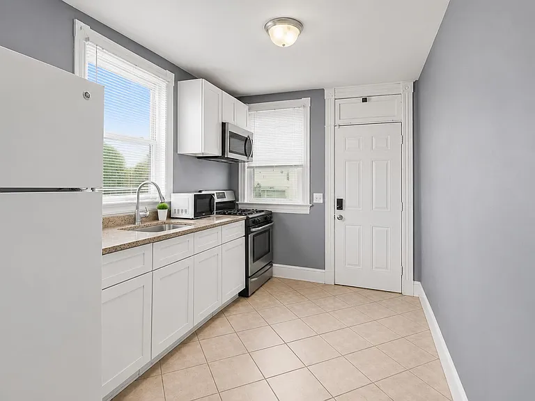Efficient kitchen with white cabinetry, tile floors, double-basin sink, and a full appliance set plus generous counter space.