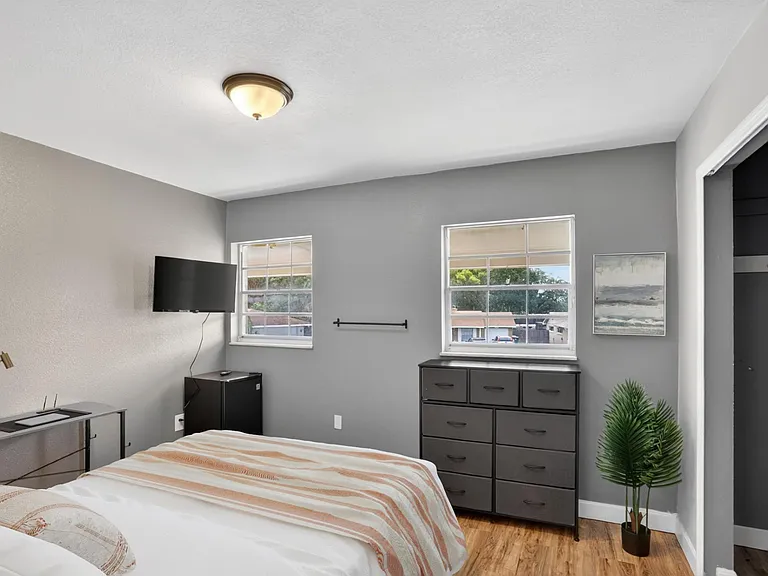 Bedroom with two windows, dresser storage, wall-mounted TV, and a dedicated desk area for work or study.