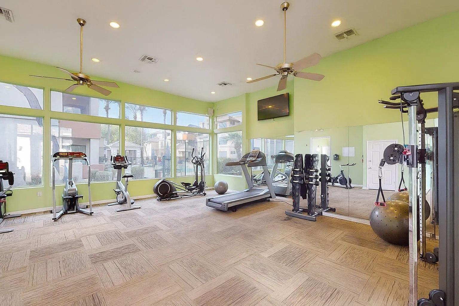Fitness center with cardio machines and free weights, large windows, and mirrors.