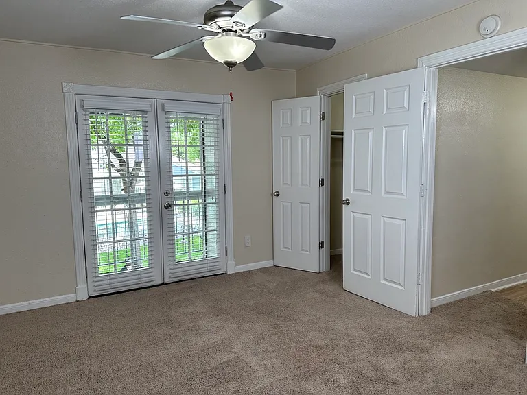 Bright bedroom with plush carpet, French doors, and a ceiling fan, offering comfort and style. Bright bedroom with plush carpet, French doors, and a ceiling fan, offering comfort and style.