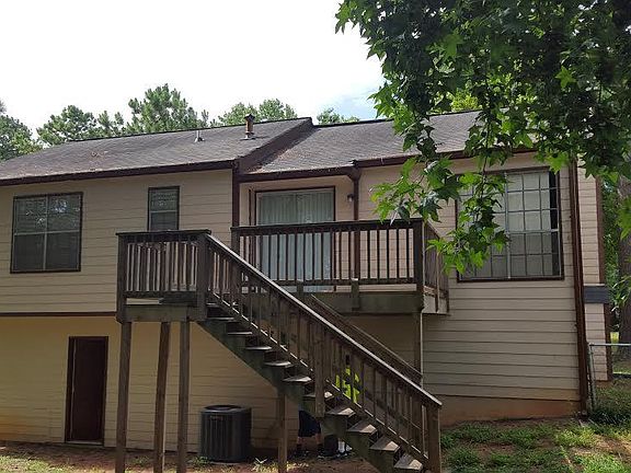Rear view of exterior showing large deck over looking mature trees with fenced yard.
