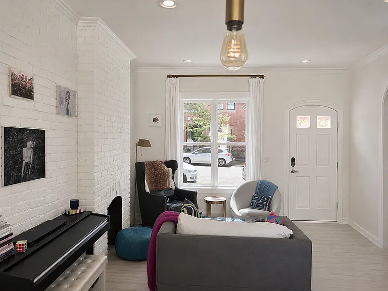 Sun-filled living room with original painted brick, oversized windows, multiple seating areas, and a warm, eclectic mix of vintage and contemporary details.
