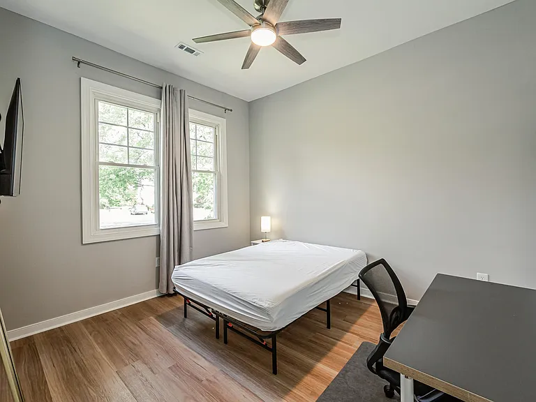 Private bedroom with two windows, ceiling fan, wood-style floors, and space for a desk or small sitting area.