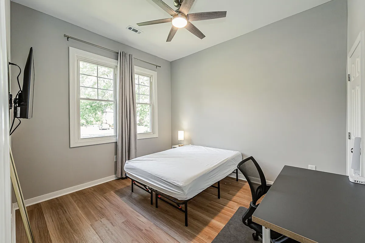 Private bedroom with two windows, ceiling fan, wood-style floors, and space for a desk or small sitting area. - Greenwood Rd