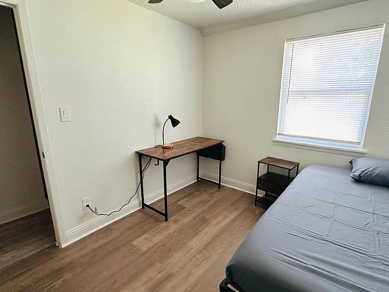 Private bedroom with wood-style flooring, a furnished work desk, and a window with blinds for comfortable everyday living.