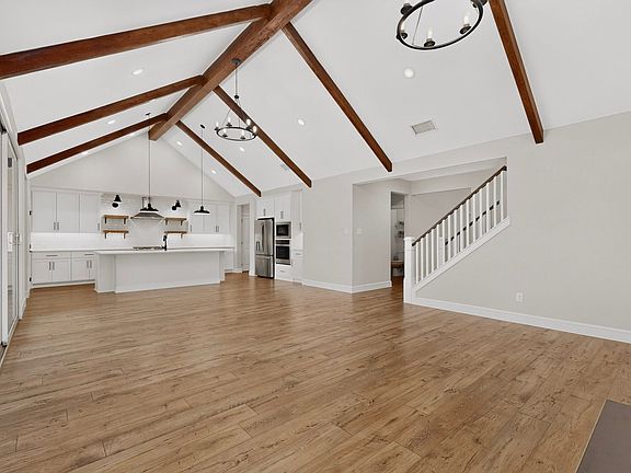 Vaulted ceilings with exposed wood beams, wood-finish flooring, white cabinetry, a kitchen island, and stainless steel appliances