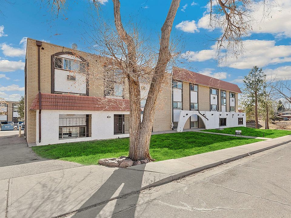 Charming apartment building with a classic red-tiled roof and well-maintained exterior, nestled in a serene neighborhood with lush green lawns and clear blue skies.