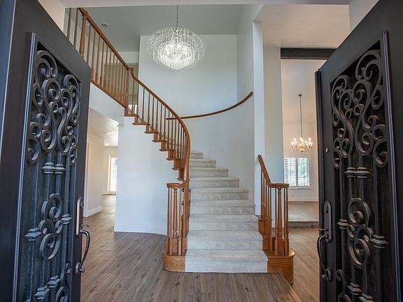Entry Hallway: Step into a grand entrance with vaulted ceilings, stunning chandelier lighting, and warm wood floors. Natural light floods the space, creating an inviting and open feel as soon as you walk in.
