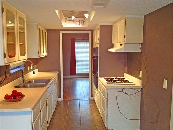 Galley style kitchen features a new sink, new lighting, updated tile floors, gas cooking and glass front cabinets