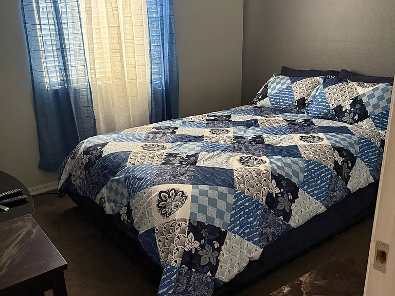 Private bedroom with a full-size bed, window with curtains, and space for a small table or dresser.
