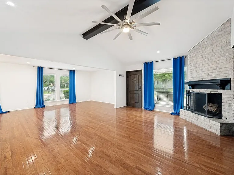 Spacious living area featuring high vaulted ceilings, wood-finish flooring, a white-painted brick fireplace, and contemporary ceiling fan