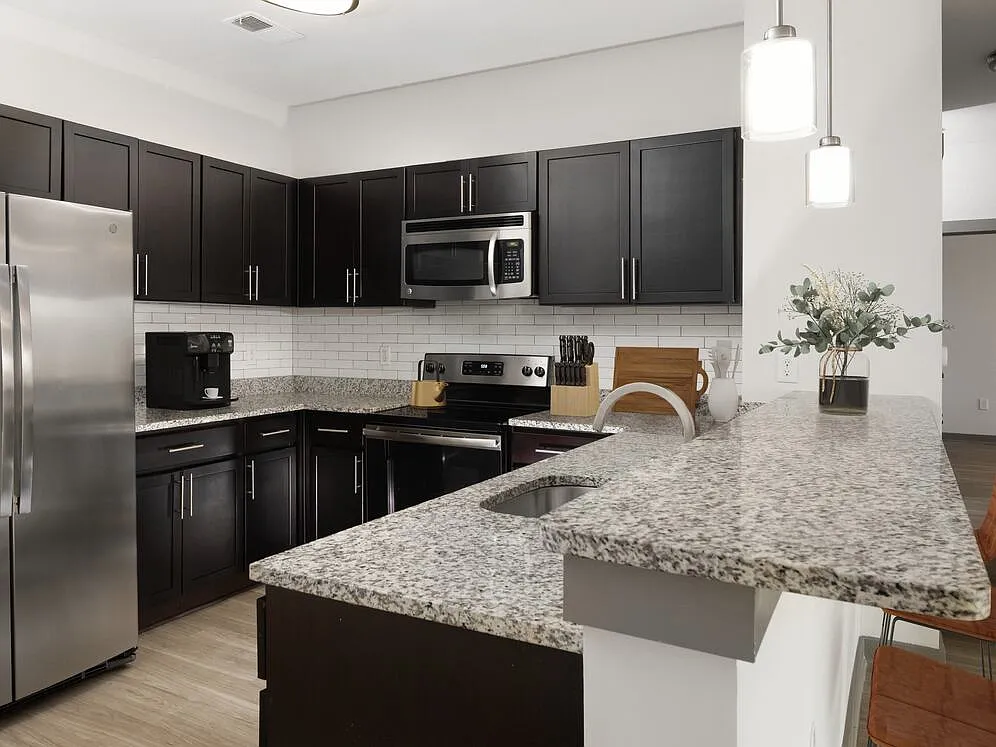 Renovated Package II Kitchen with dark cabinetry, speckled granite countertops, white tile backsplash, stainless steel appliances, pendant lighting, and hard surface flooring - AVA South End