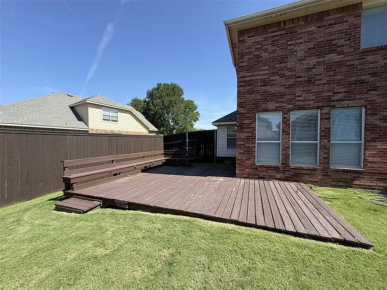 BACK OF THE HOUSE WITH LARGE WOOD DECK WITH SEATING.