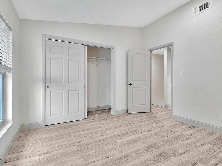 Bright bedroom with elegant wood flooring, large window for natural light, and spacious closet.