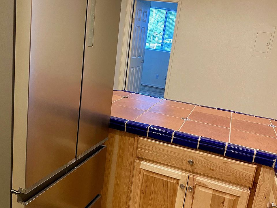 View across wide eat in counter top (overhang on other side), new floors, new cabinets, new light fixtures, new deluxe refrigerator
