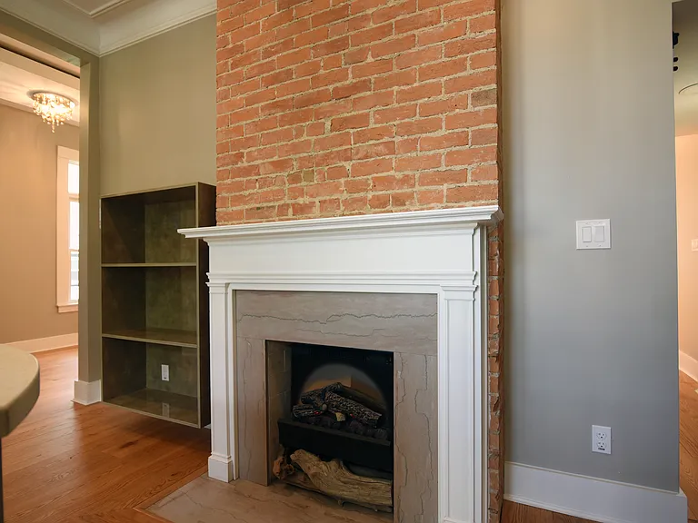 Suspended book/display case next to restored and exposed brick electric log fireplace. Original marble hearth and surrounds with mantle.