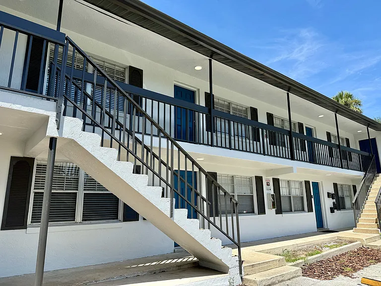 Bright and inviting two-story apartment building with modern railings, spacious balconies, and a sleek exterior under a clear blue sky.