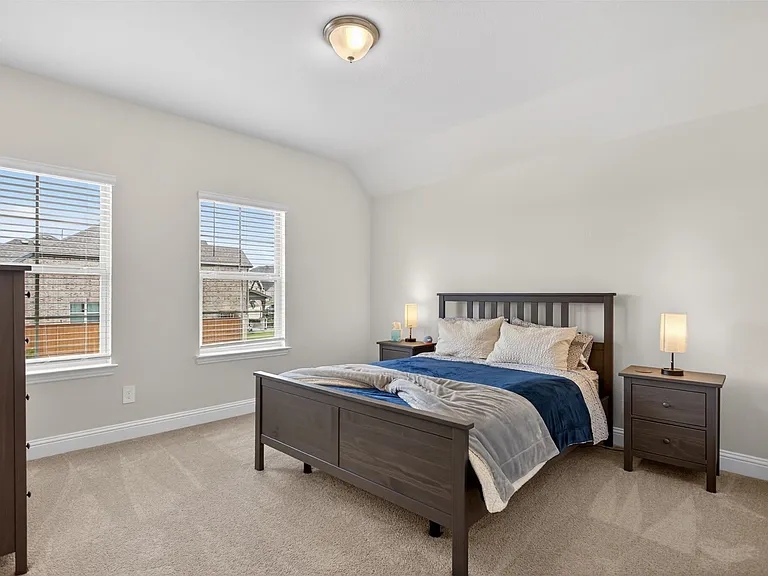 Carpeted bedroom featuring two large windows with blinds, a neutral wall color, and a ceiling-mounted light fixture