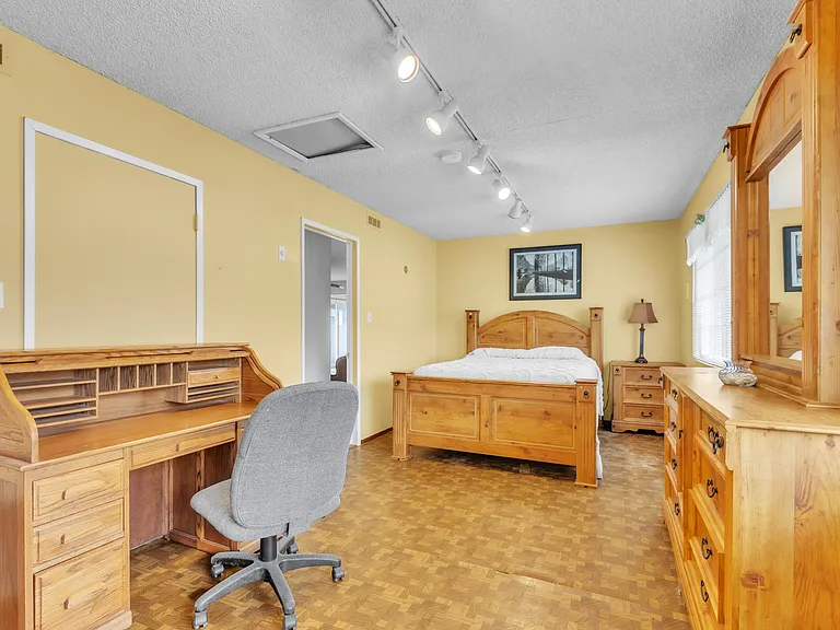 Bedroom with King bed and workspace. Full dresser with a mirror. Wooden floors. View of the front yard.