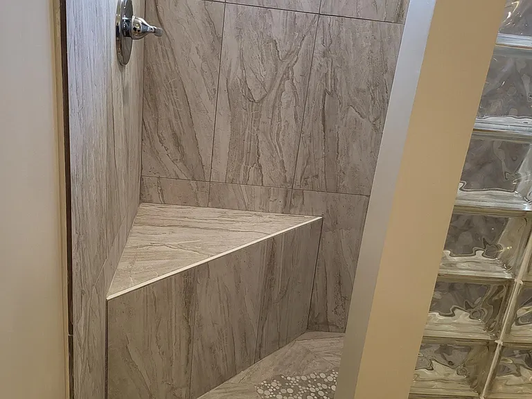 Shower with sitting area, rainfall shower fixture and design, glass block, and a private glass window to let in natural light.