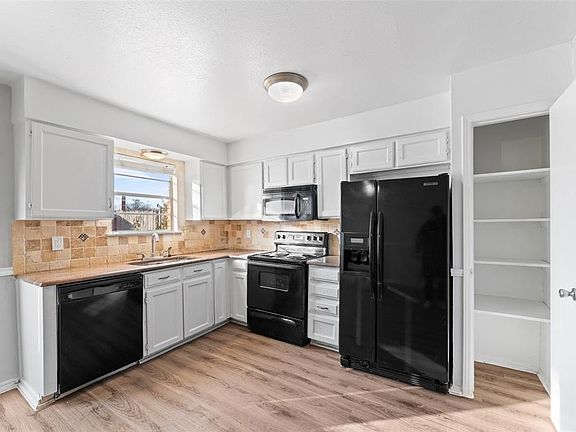 Kitchen with black appliances, light countertops, light wood finished floors, decorative backsplash, and white cabinets