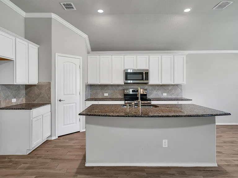 Kitchen featuring a central island with an undermount sink, white cabinetry, dark speckled countertops, and a tiled backsplash
