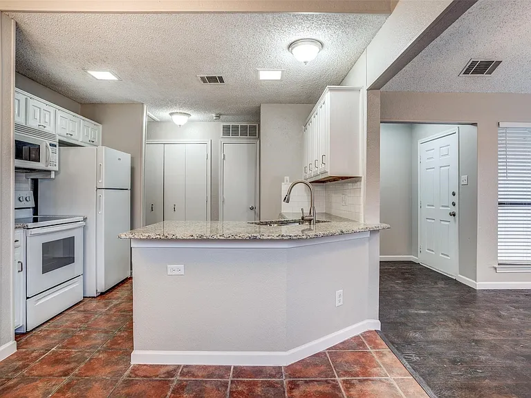 Kitchen features granite counters, white cabinets & includes fridge.