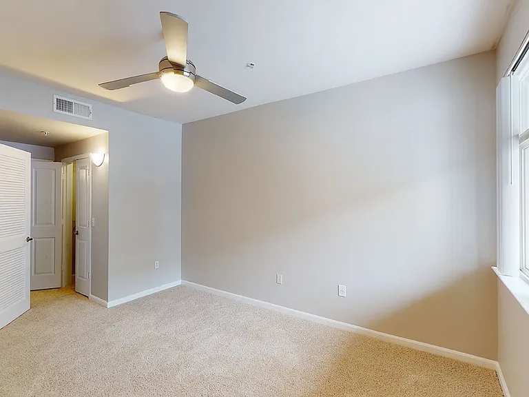 Spacious apartment bedroom with large closet, attached bathroom and plush carpet flooring.