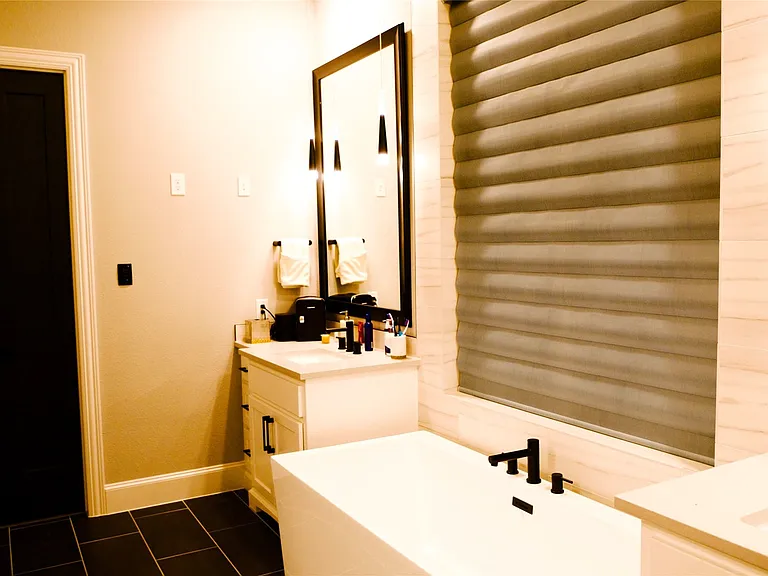 Modern bathroom featuring a freestanding tub with matte black fixtures, dual vanities with undermount sinks and quartz countertops, and a large window with horizontal blinds