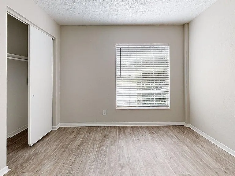 Bright bedroom with elegant laminate flooring and a large window casting natural light.