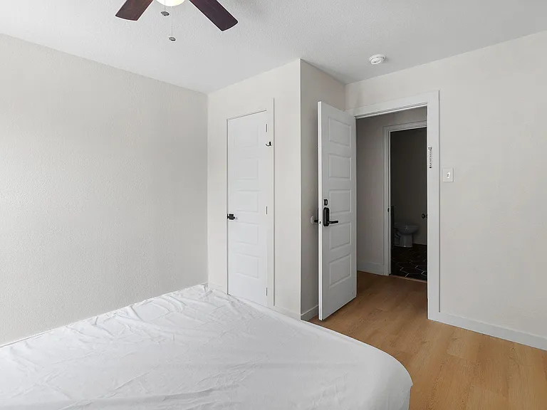 Private bedroom with wood-style flooring, ceiling fan, and quick access to an adjacent bathroom for added convenience.