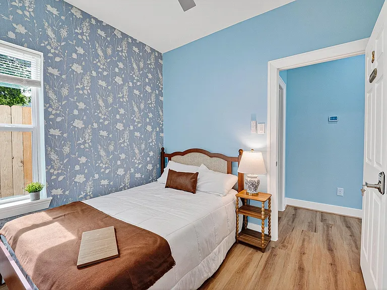 Inviting bedroom featuring a queen bed, patterned accent wall, and a large window with blinds for natural light and privacy.