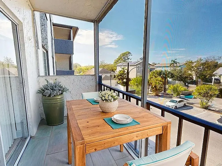 Charming balcony with a cozy wooden dining table, lush greenery, and an inviting view of a sunny neighborhood.