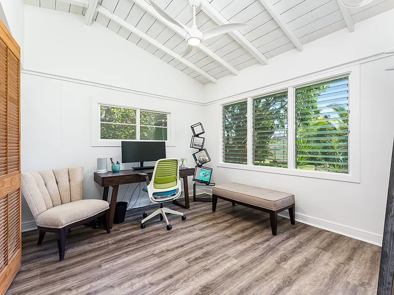 Bedroom 3 with vaulted ceilings, abundant natural light, and an ensuite bathroom. Currently staged as a home office with views overlooking the landscaped yard.